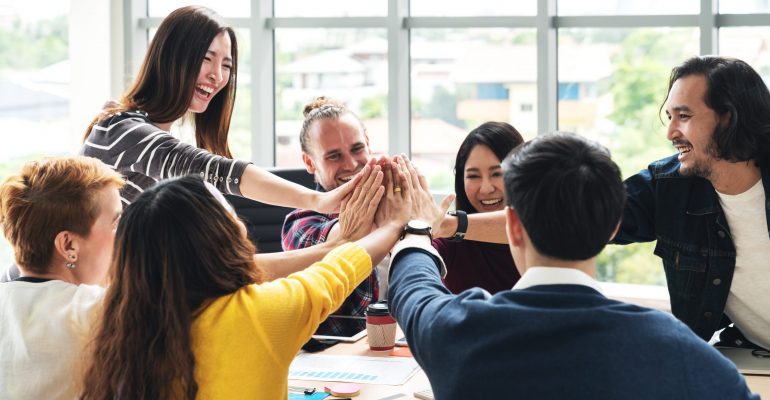 group of young multiethnic diverse people gesture hand high five, laughing and smiling together in brainstorm meeting at office. Casual business with startup teamwork community celebration concept.